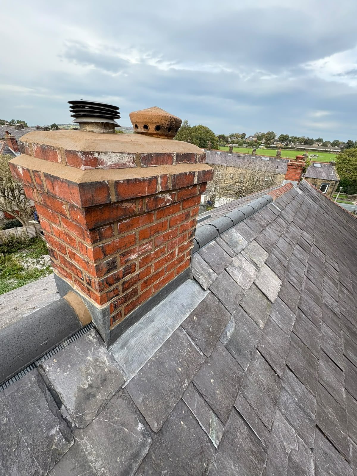 Rebuilt red brick chimney stack with new clay pots and fresh lead flashing on a slate roof in East Lancashire